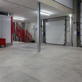 Moderner Lagerraum mit Rolltoren, roter Treppe und abgeschlossenen Selfstorage-Boxen.