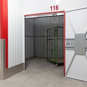 Moderner Selfstorage-Lagerraum mit geöffneter Tür und Transportwagen im Innenbereich.