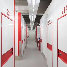 Gang mit modernen Selfstorage-Lagerräumen, rote und weiße Türen, helle Beleuchtung.