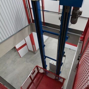 Lastenaufzug mit rotem Korb und blauen Streben in moderner Lagerhalle von oben.